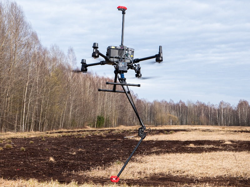 A DJI drone carrying the MagNIMBUS dual-sensor magnetometer system over a field