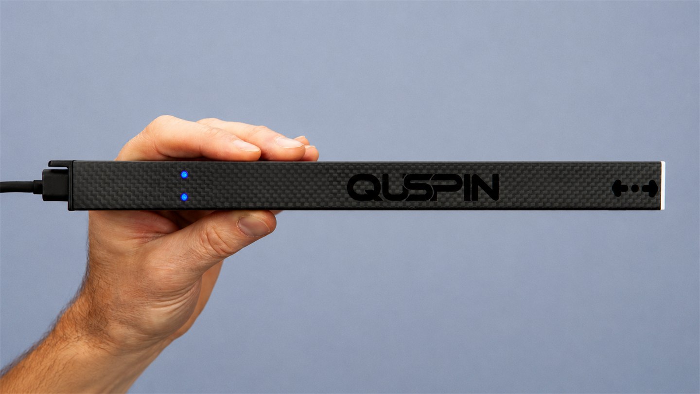 A Magpie in a carbon-fiber housing held in one hand, showing its two blue status LEDs