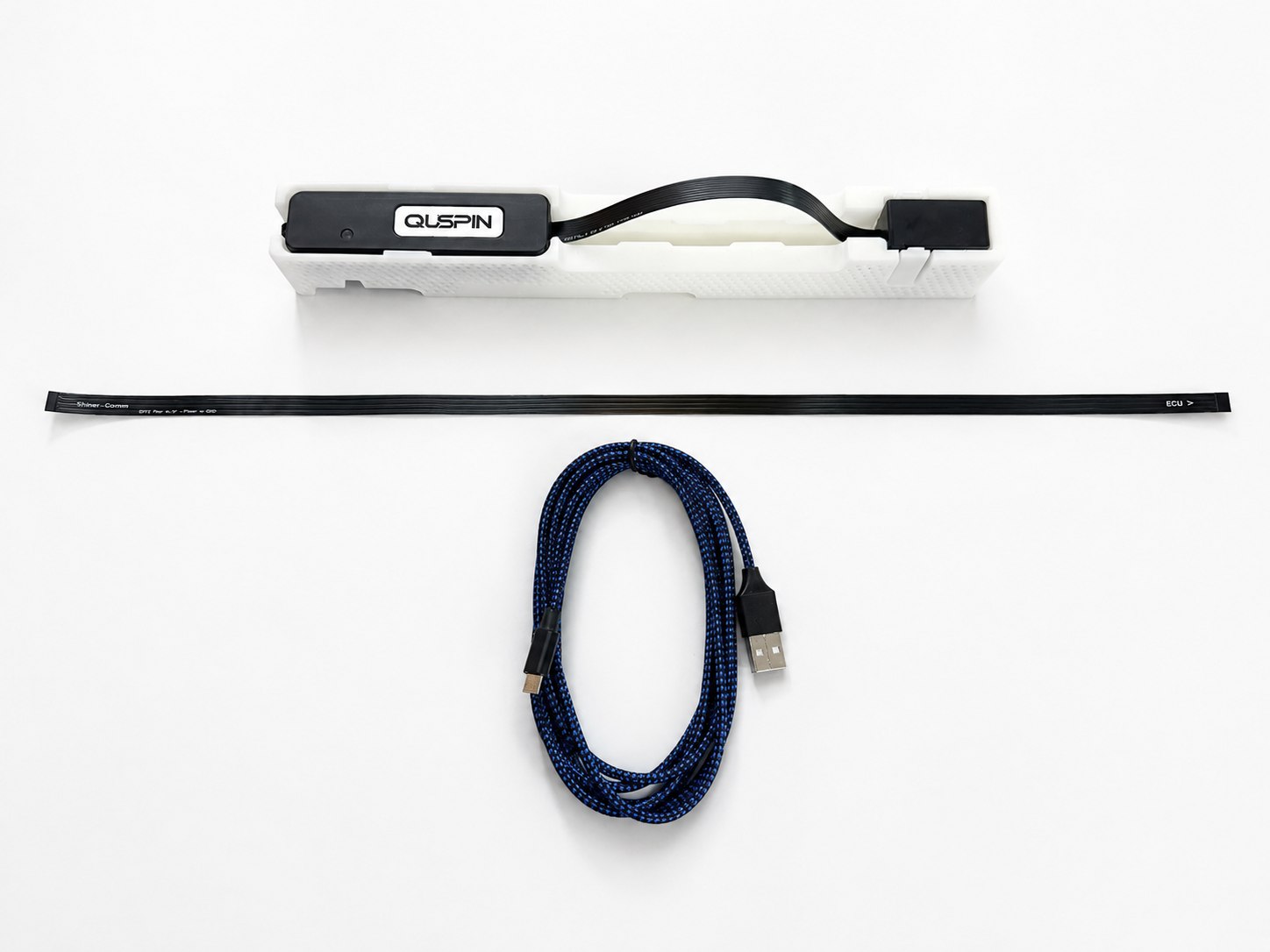 The standalone QTFM Gen-2 package on a white background: the sensor head and Electronics Control Unit in their carrier, the flat power and comms flex cable, and the braided USB interface cable. The Standard Comms Board is under the ECU and is not visible.
