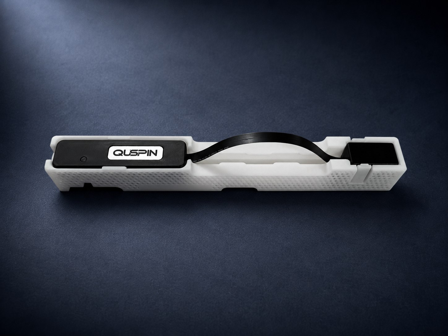 QTFM Gen-2 sensor head and Electronics Control Unit seated in the white carrier that holds them together, joined by a black flex cable. The Standard Comms Board sits beneath the electronics and is not visible.
